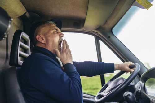 Mature truck diver feeling tired and yawning during the ride. Concept for Truck Driver Fatigue: Drowsy Truck Drivers Put Others at Risk.