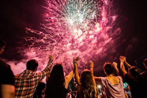 Back view of large group of people watching fireworks on the sky by night. Visual concept for a personal injury blog discussing: Ann Arbor fireworks regulations, approved types, and crucial safety advice to prevent injuries and accidents.